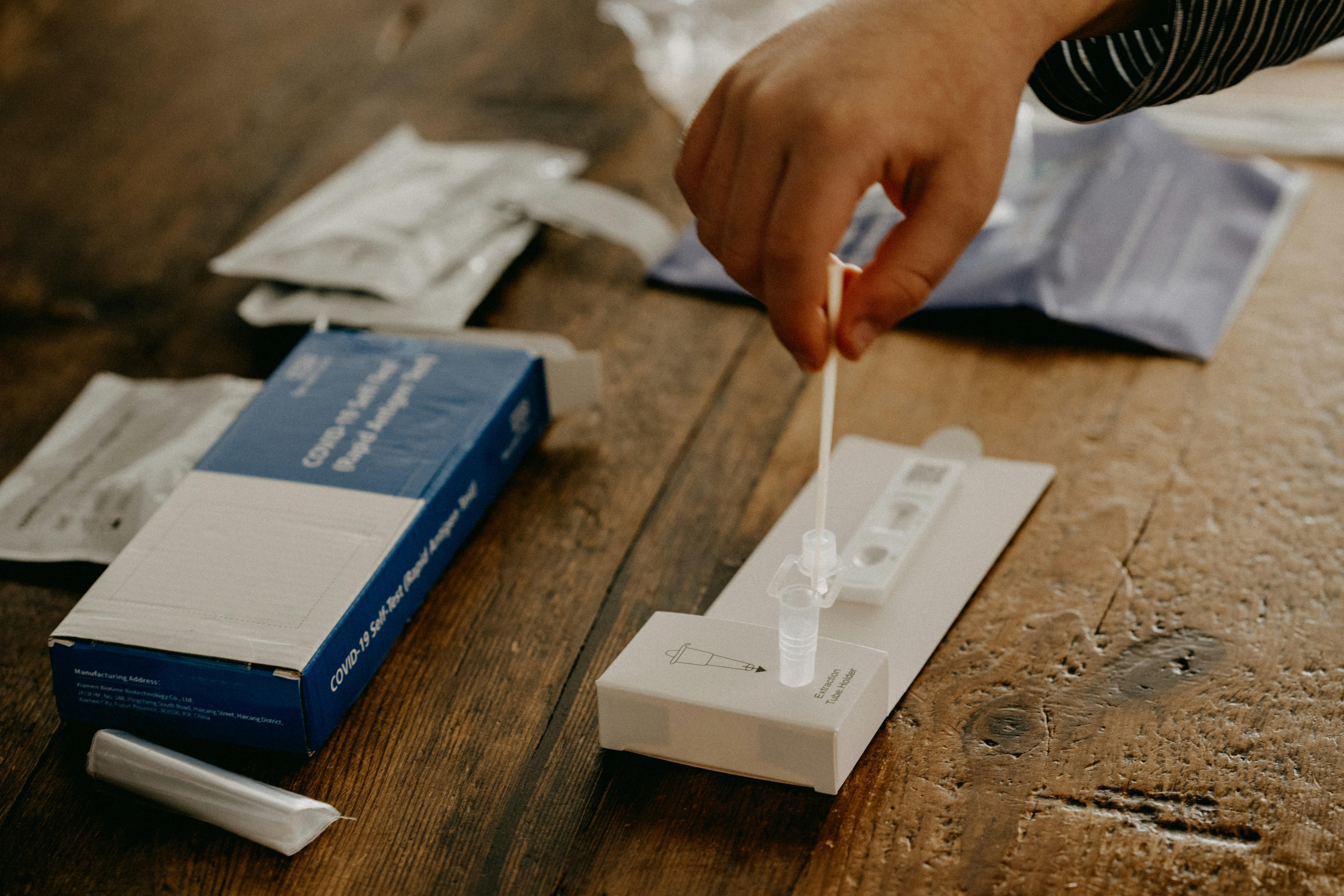 A patient is taking a COVID test with part of the test displayed on a tabletop.